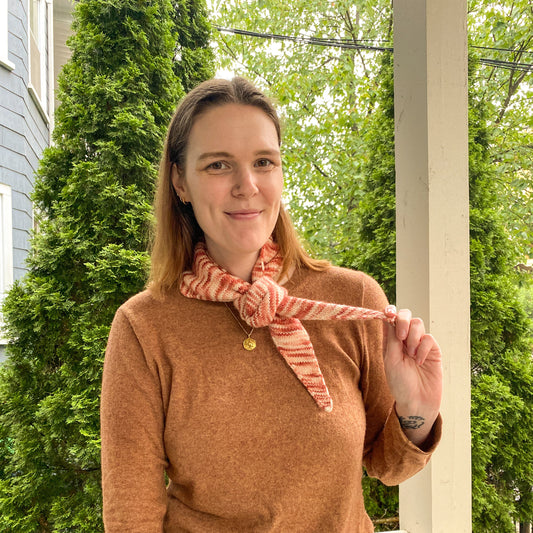 Woman holding a variegated pink knitted bandana scarf outdoors on a porch