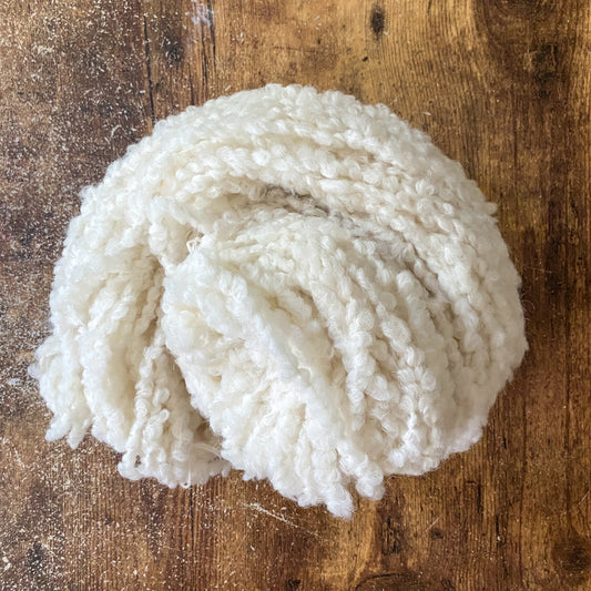 Ball of bulky undyed alpaca/wool boucle yarn on a wooden surface
