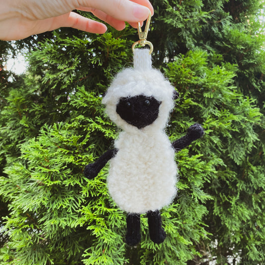 Hand holding a sheep-shaped keychain against a green tree background