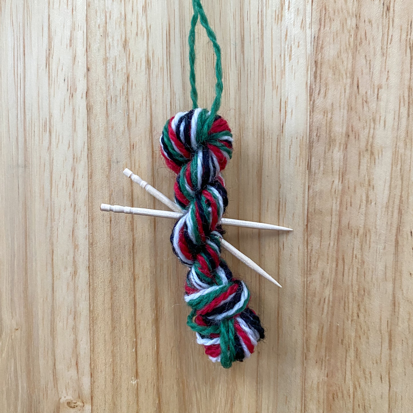 mini yarn skein ornament with toothpick knitting needles in red, green, black, and white