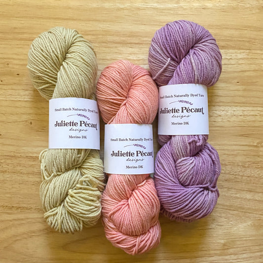 3 skeins of merino wool yarn in green, coral, and purple