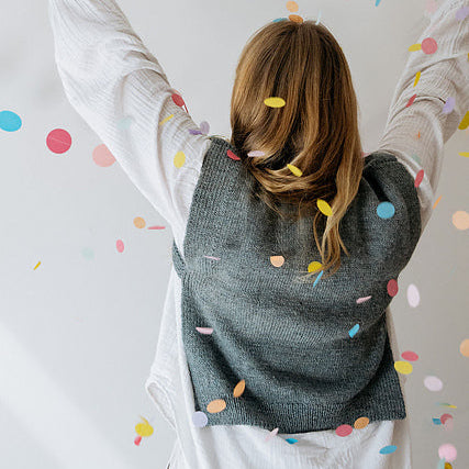 Person wearing a gray knitted vest with colorful confetti falling around them on a light background