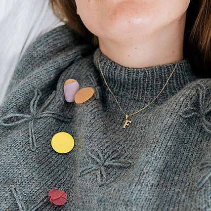 Gray sweater with colorful confetti and a gold necklace with a 'F' pendant.
