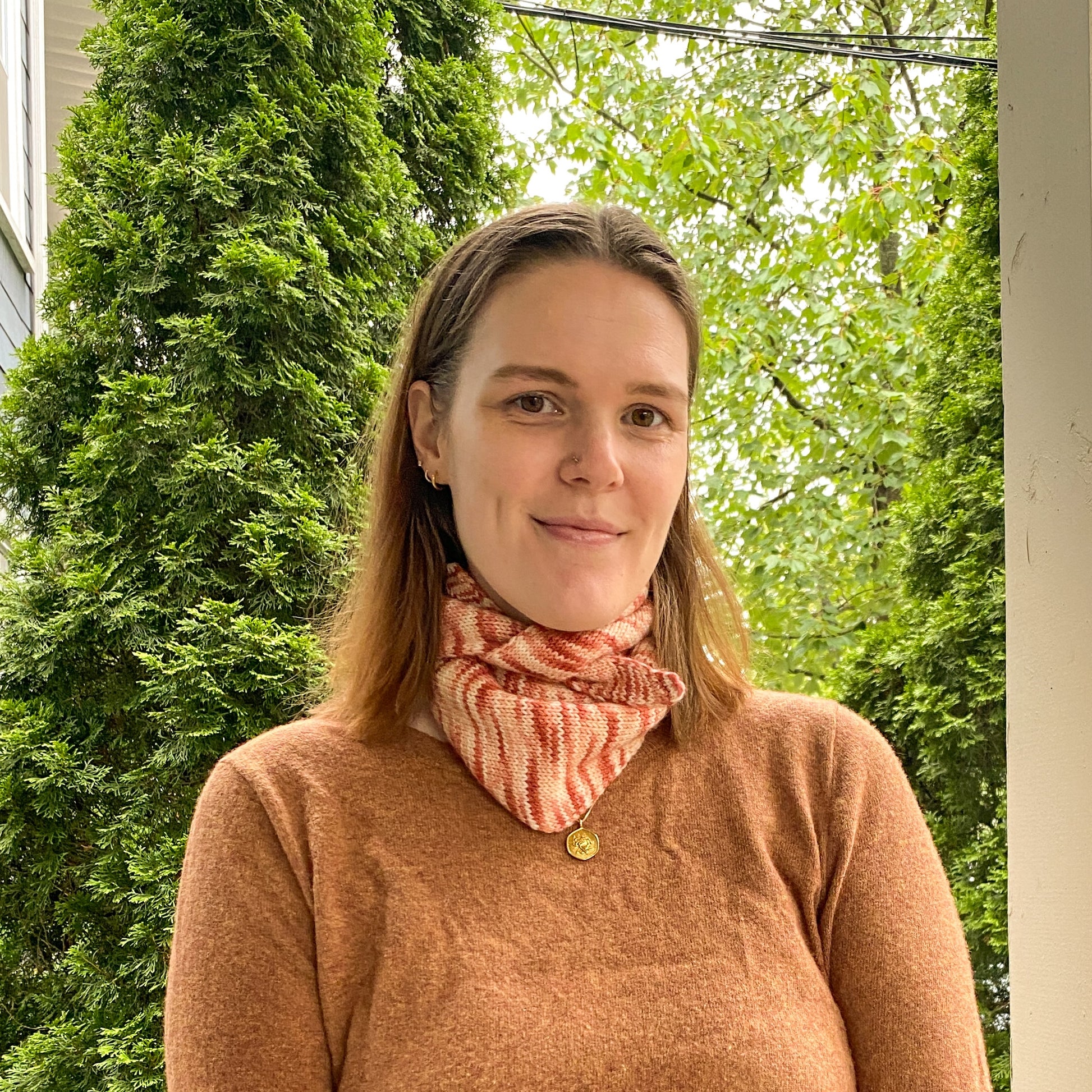 Woman wearing a variegated pink knitted scarf outdoors with greenery in the background
