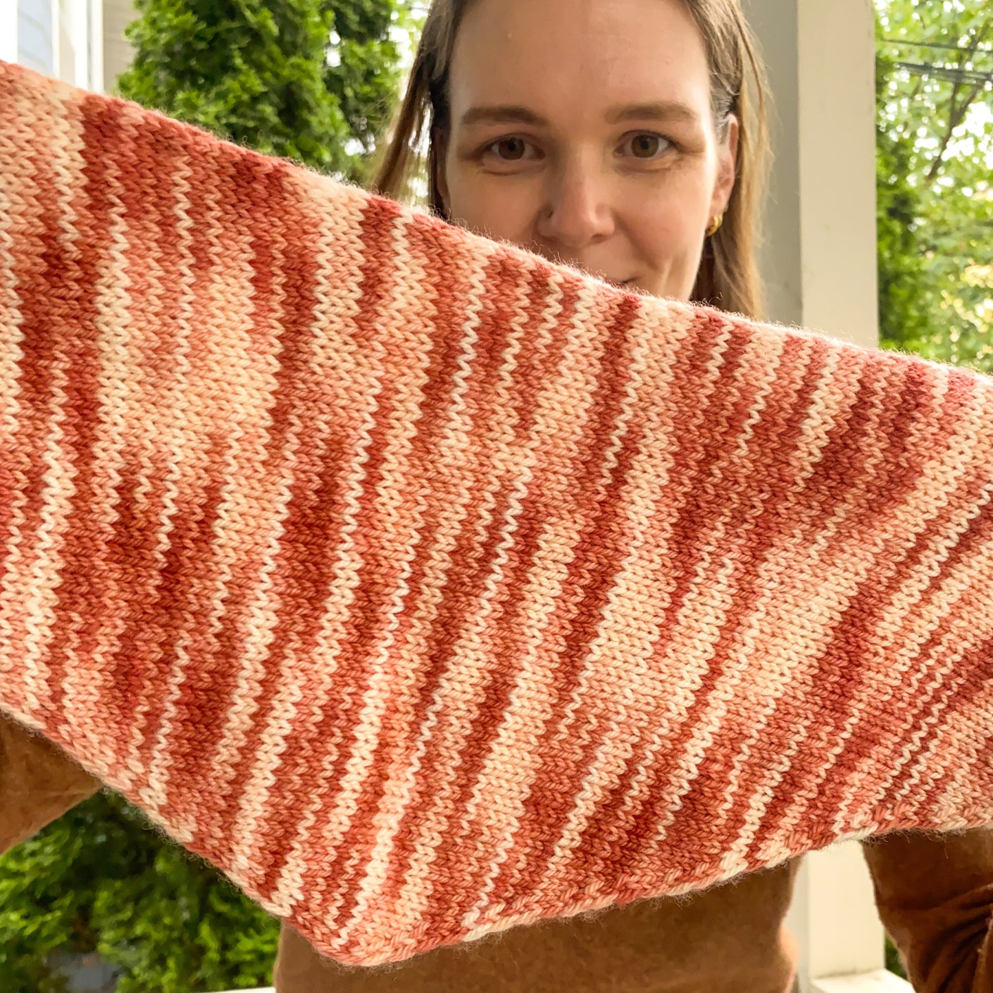 Person holding a pink knitted triangle scarf with a blurred background