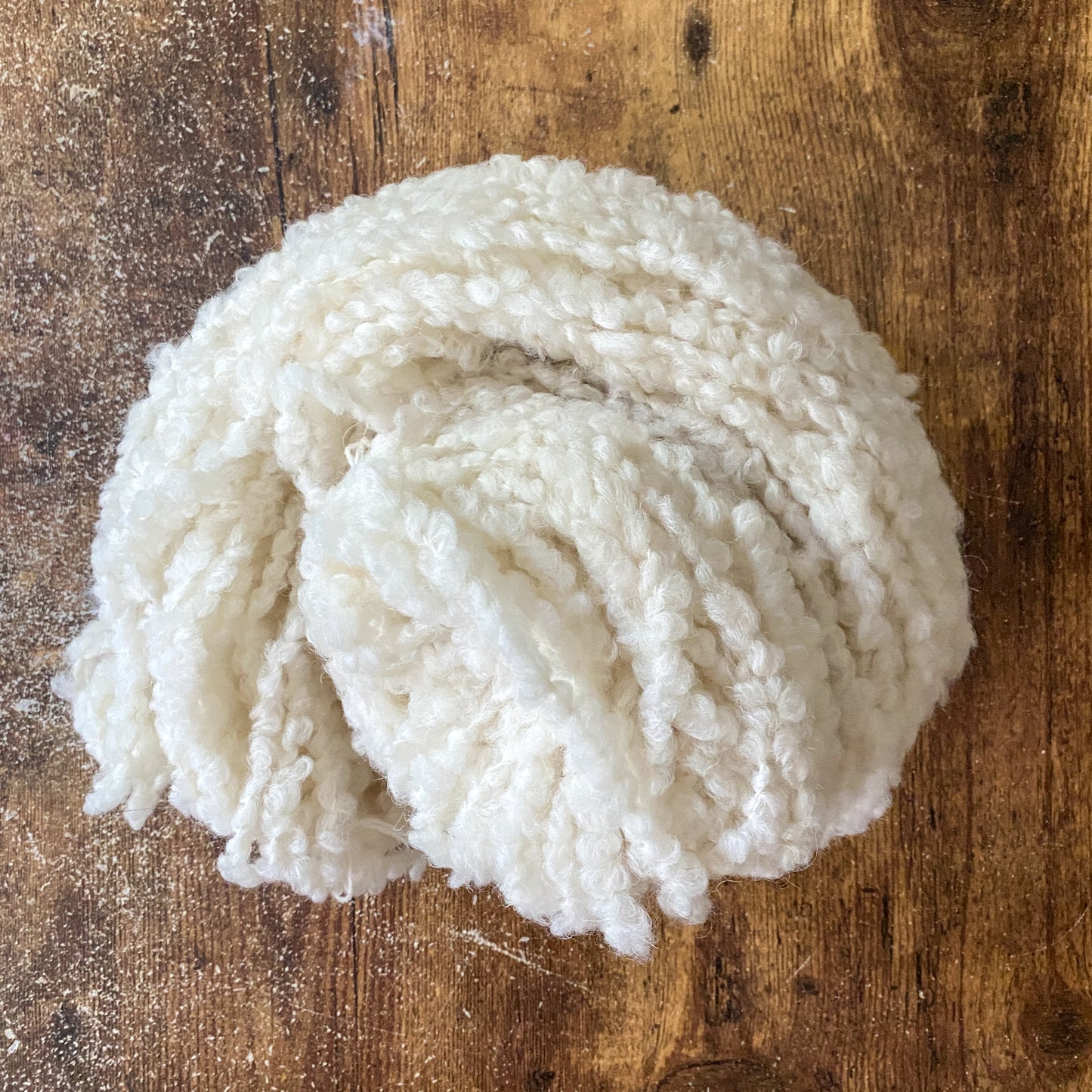 Ball of bulky undyed alpaca/wool boucle yarn on a wooden surface