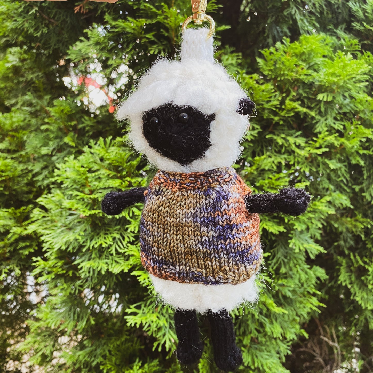 Knitted sheep keychain held against a green leafy background