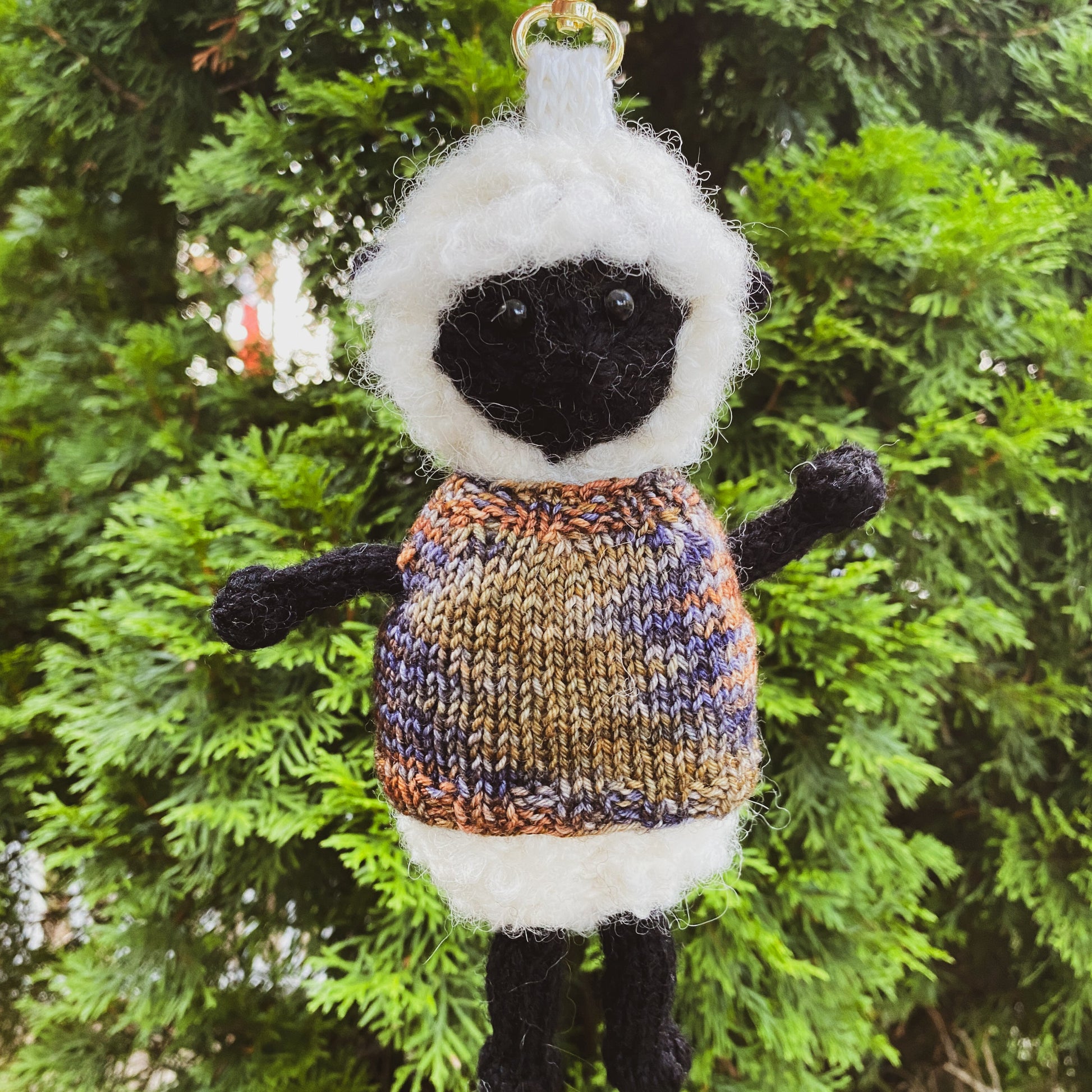 Knitted sheep keychain with a sweater against a green leafy background