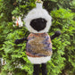 Knitted sheep keychain with a sweater against a green leafy background