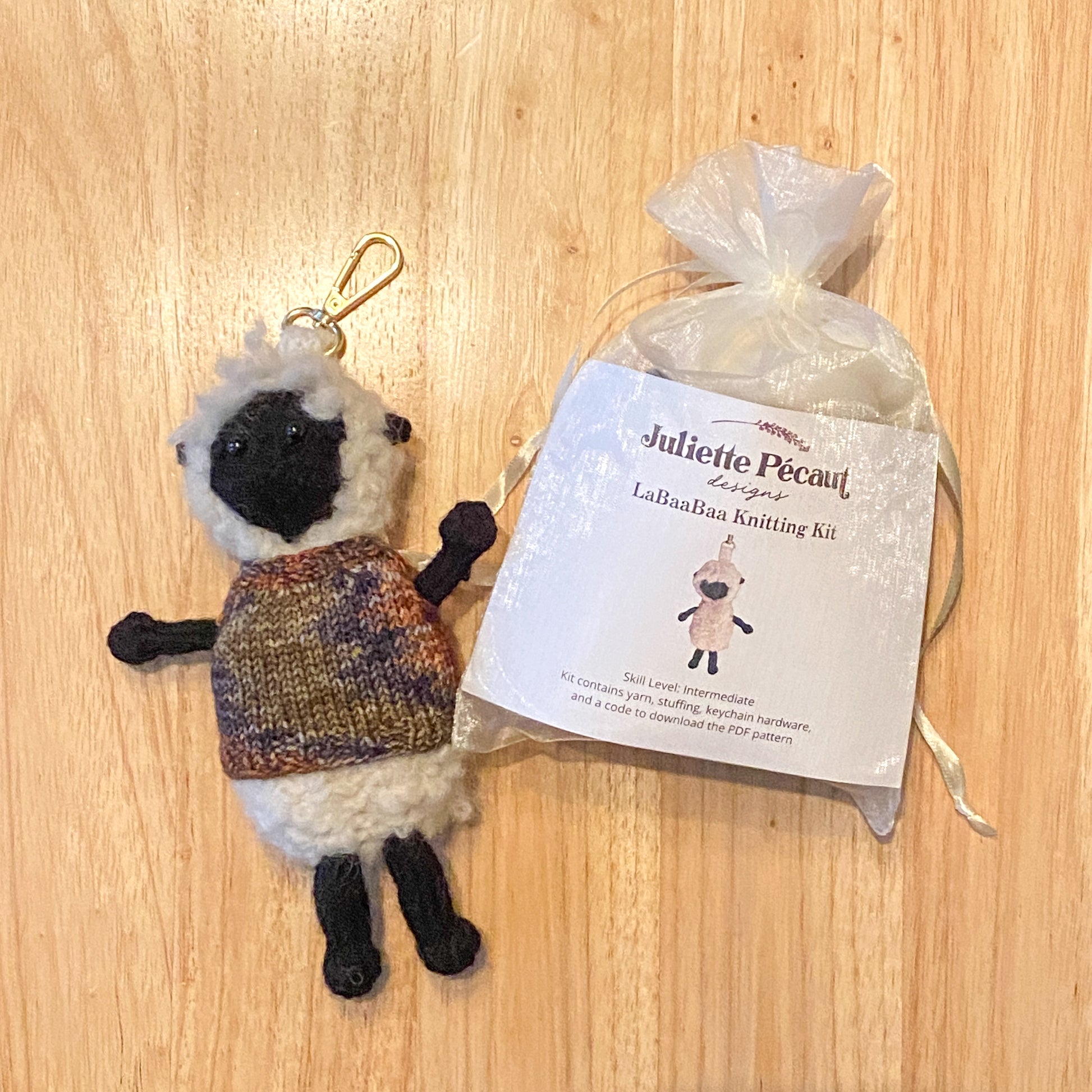 Knitted sheep keychain with a Juliette Pecaut knitting kit on a wooden surface