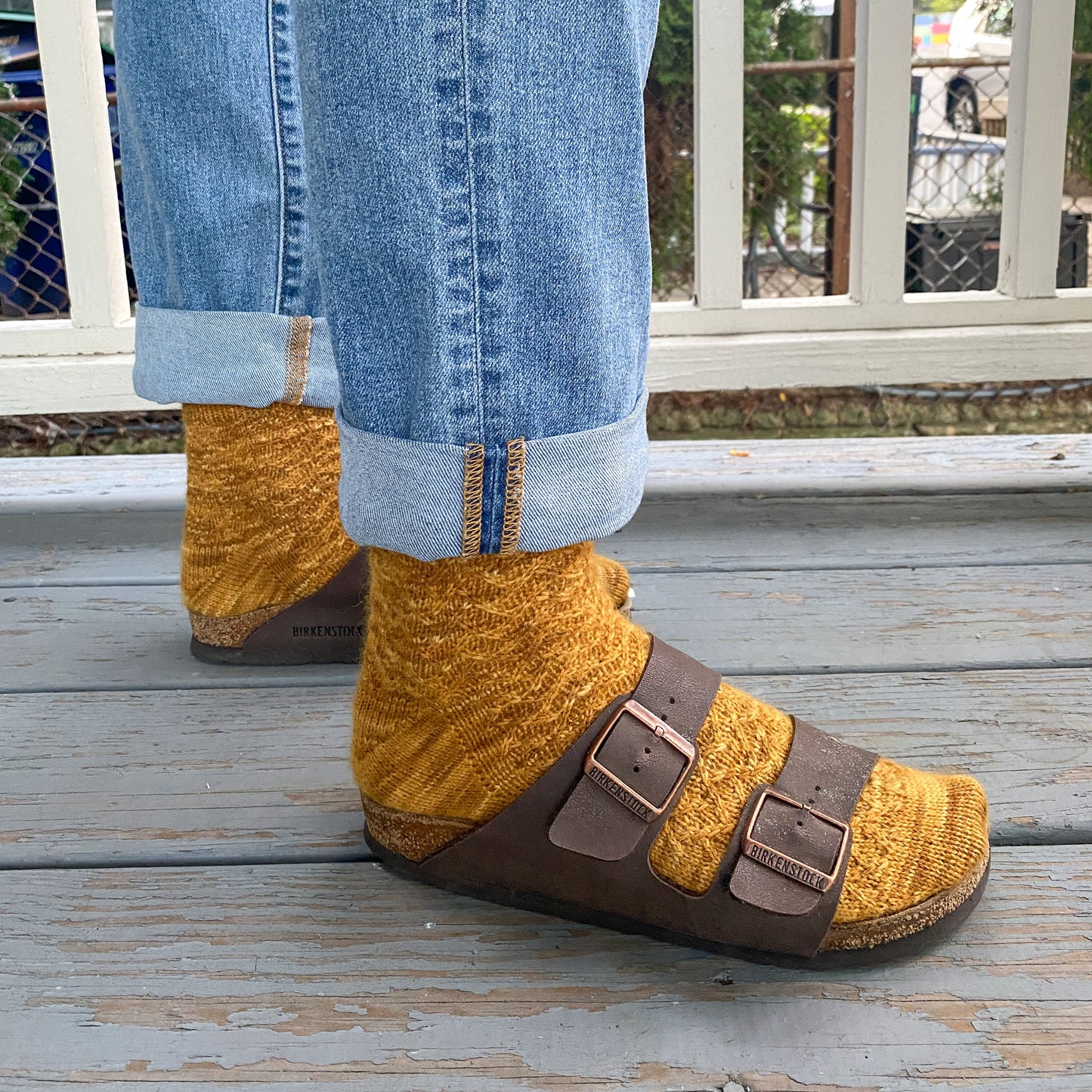Person wearing mustard yellow socks with brown sandals on a wooden deck.