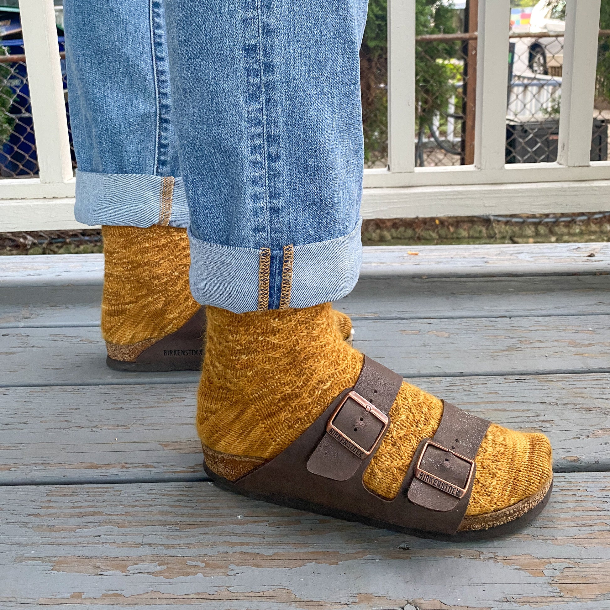 Person wearing mustard yellow socks with brown sandals on a wooden deck.