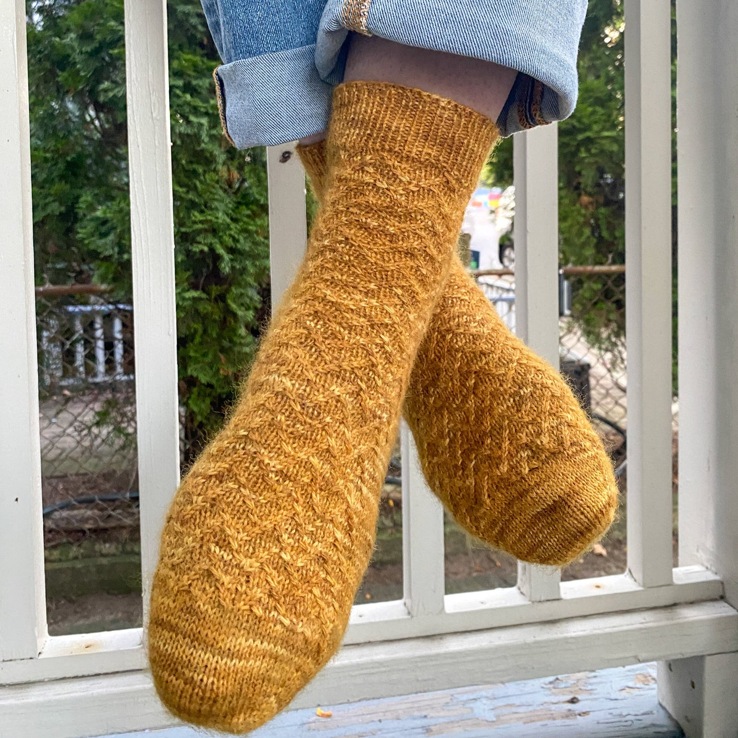 Person wearing mustard yellow knitted socks with rolled-up blue jeans on a porch.