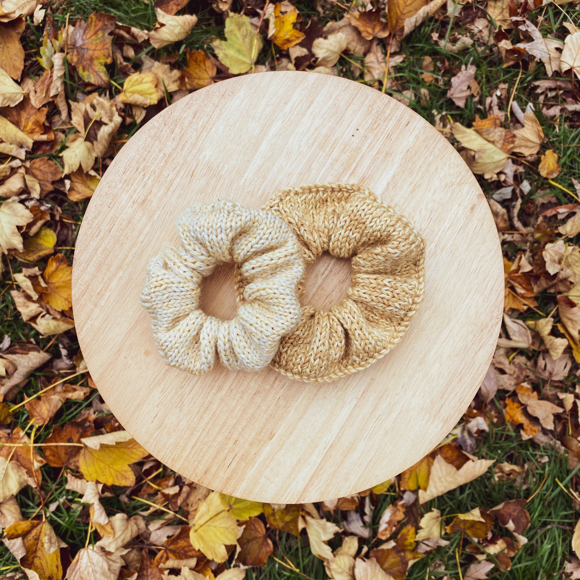 Two scrunchies on a wooden board surrounded by autumn leaves.