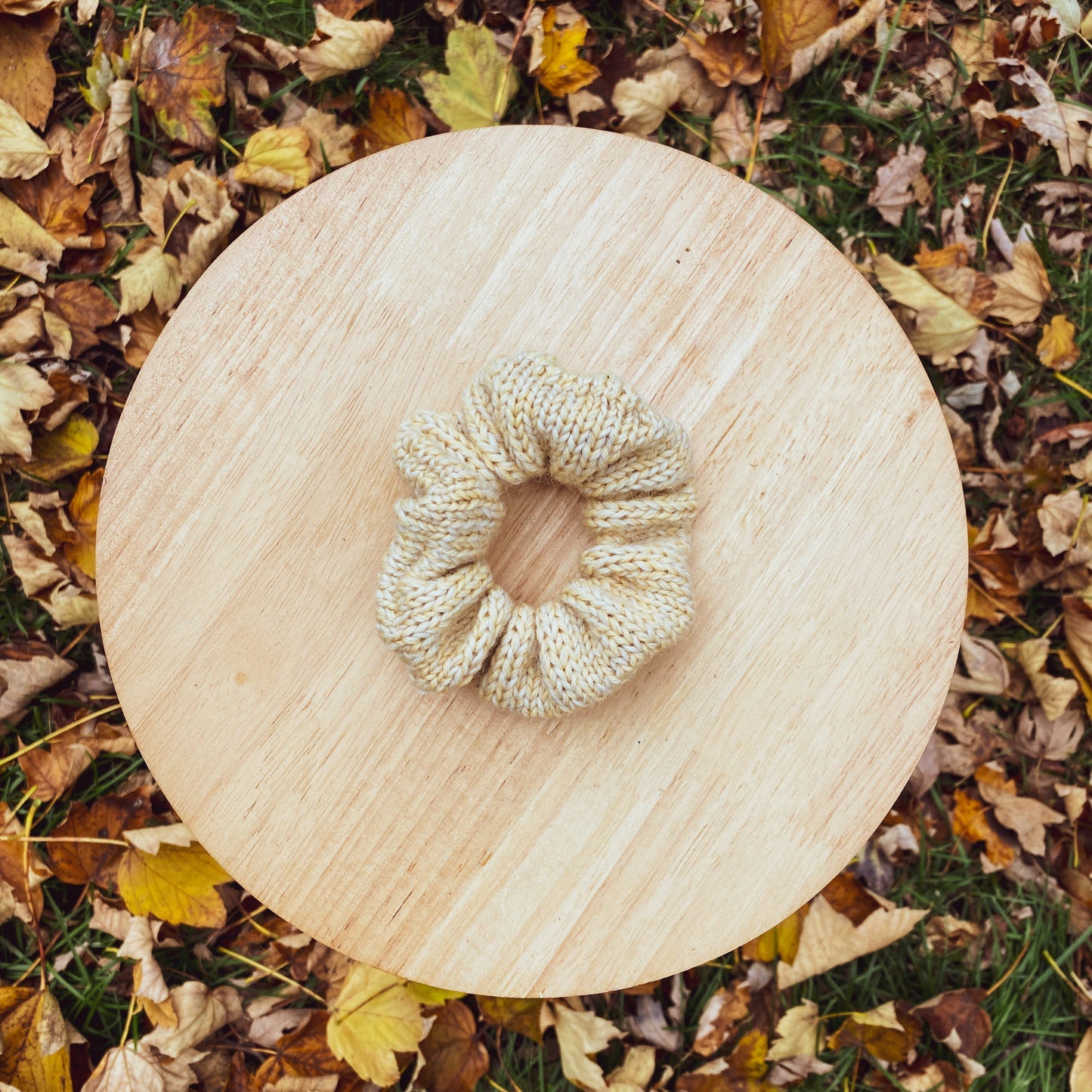 Knitted scrunchie on a wooden board with autumn leaves in the background