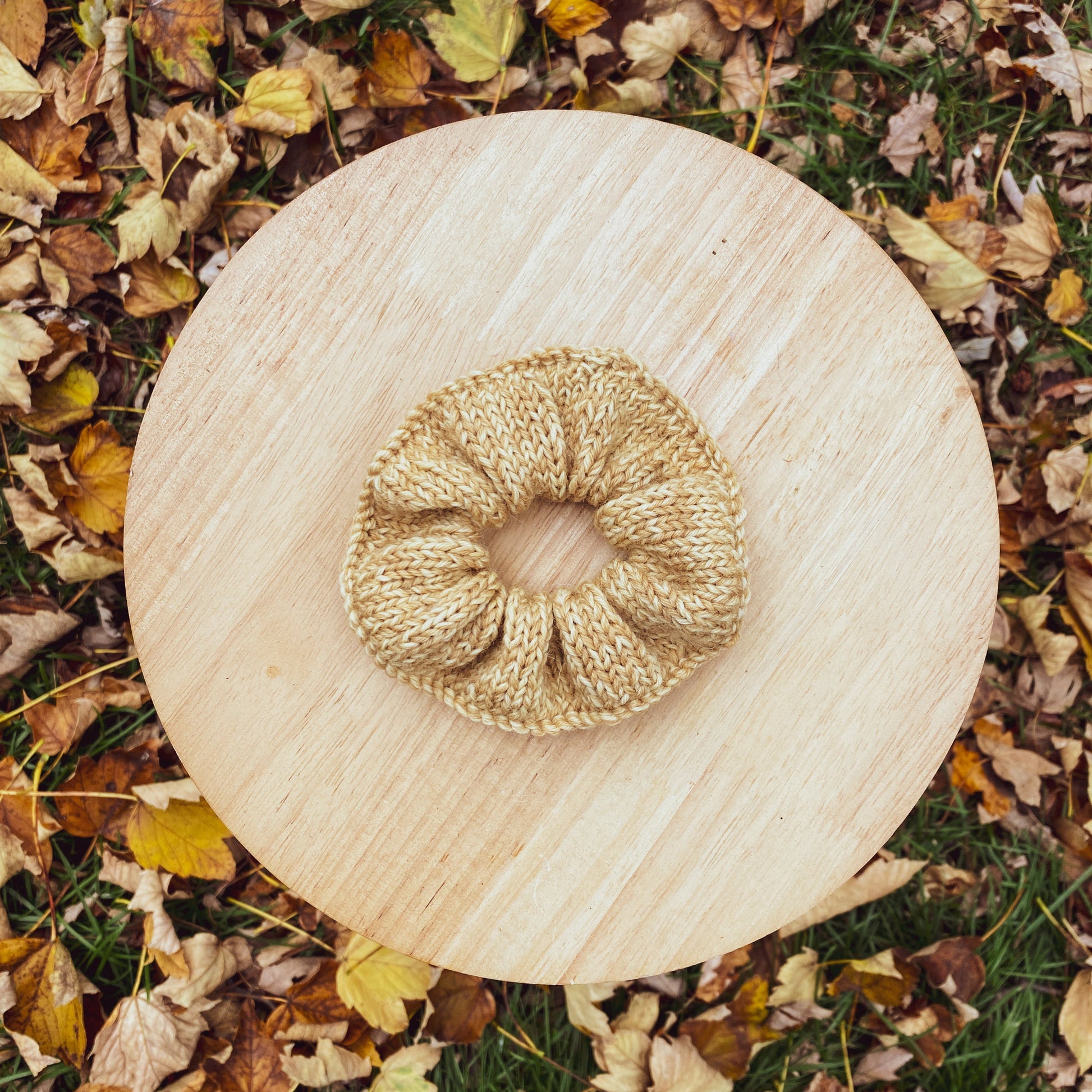 Knitted scrunchie on a wooden stool surrounded by autumn leaves