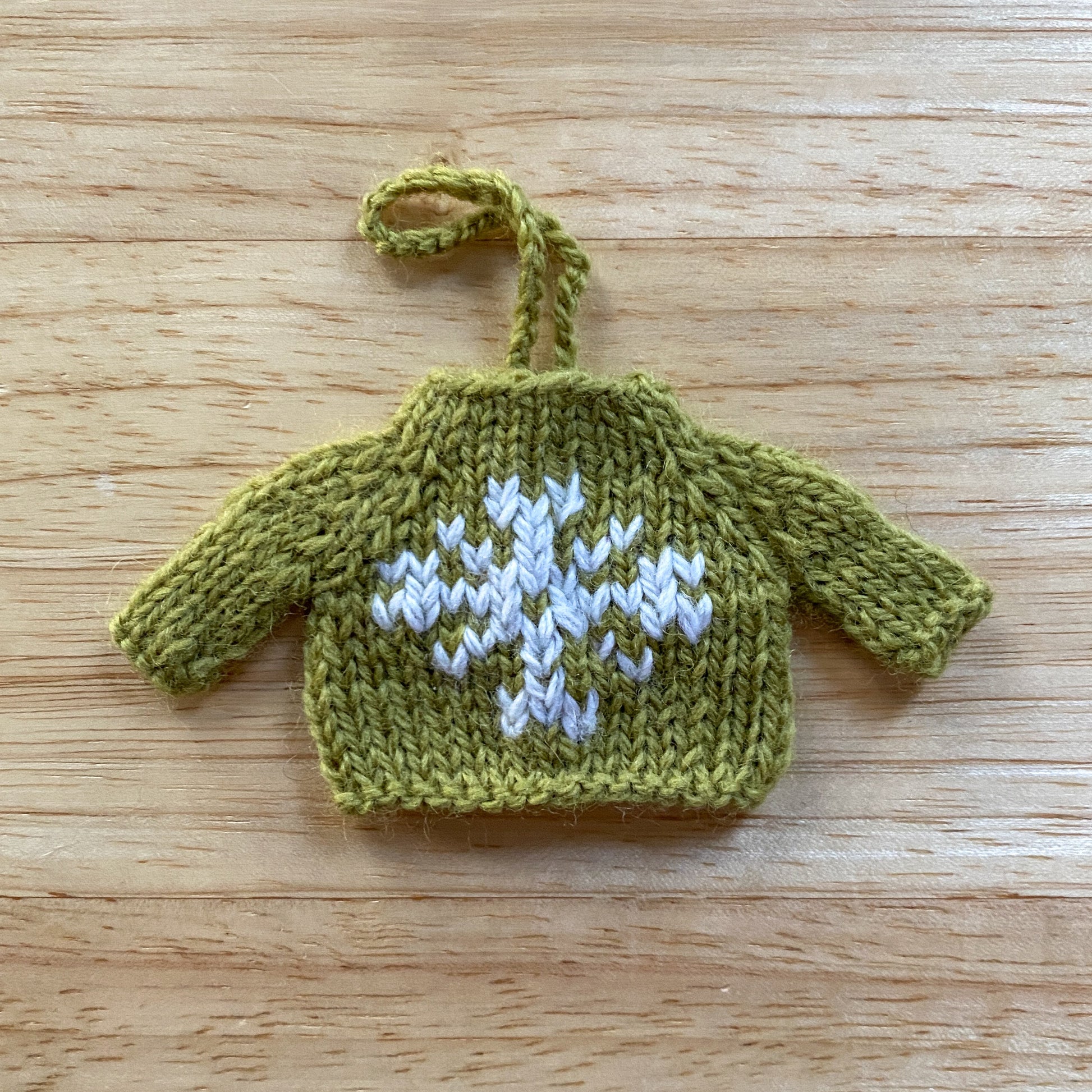mini green knitted sweater ornament with a white snowflake embroidered on the front