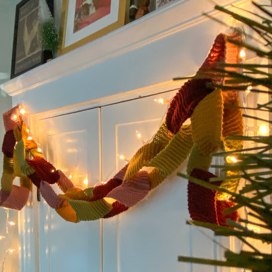 Decorative knitted garland on a door with framed photos in the background.