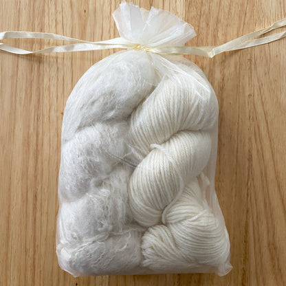 Two skeins of white yarn in a clear organza bag on a wooden surface