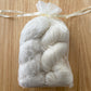 Two skeins of white yarn in a clear organza bag on a wooden surface