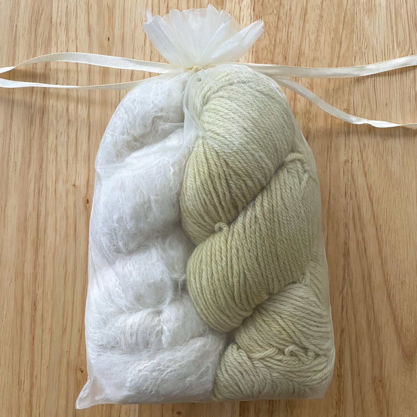 A fluffy white skein of yarn and a lime green skein of yarn in a clear organza bag on a wooden surface