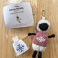 Knitted sheep keychain with sweater, knitting kit packaging, and pattern chart on a wooden surface.