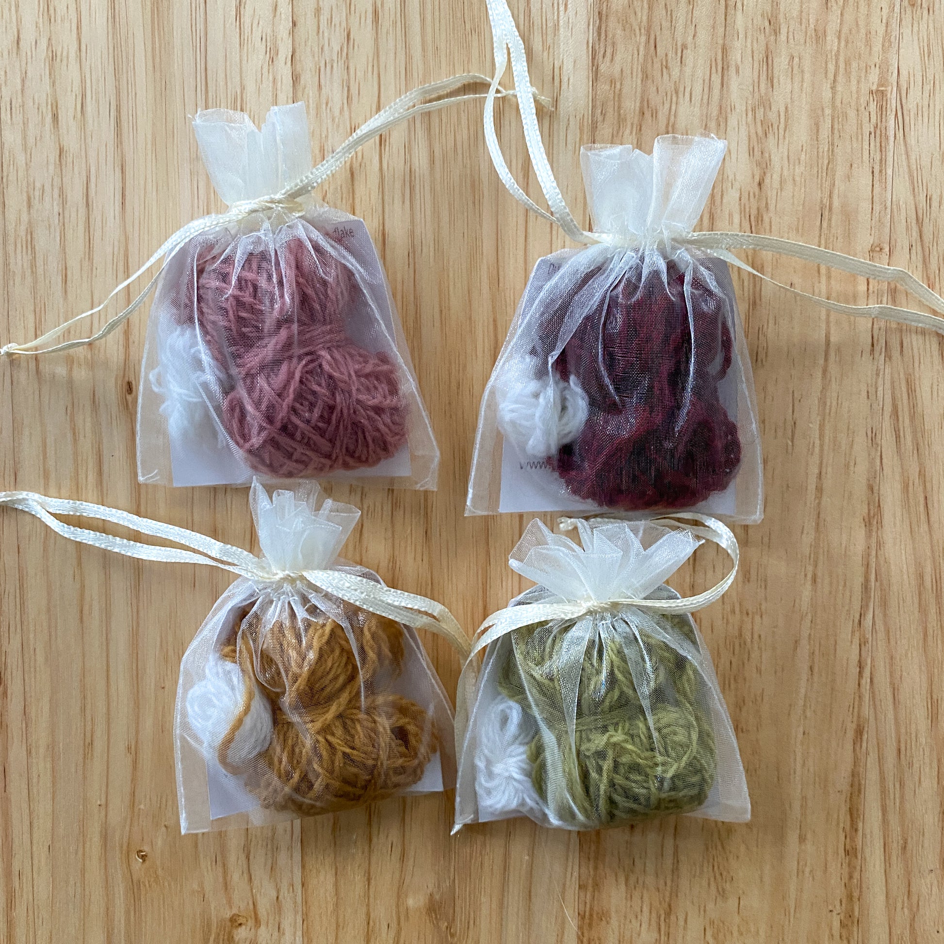 Four small clear bags with yarn balls tied with ribbons on a wooden surface