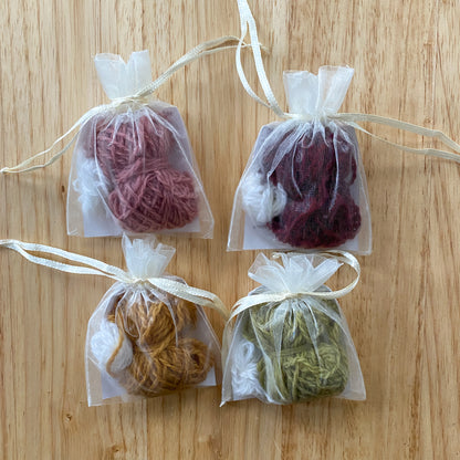 Four small clear bags with yarn balls tied with ribbons on a wooden surface