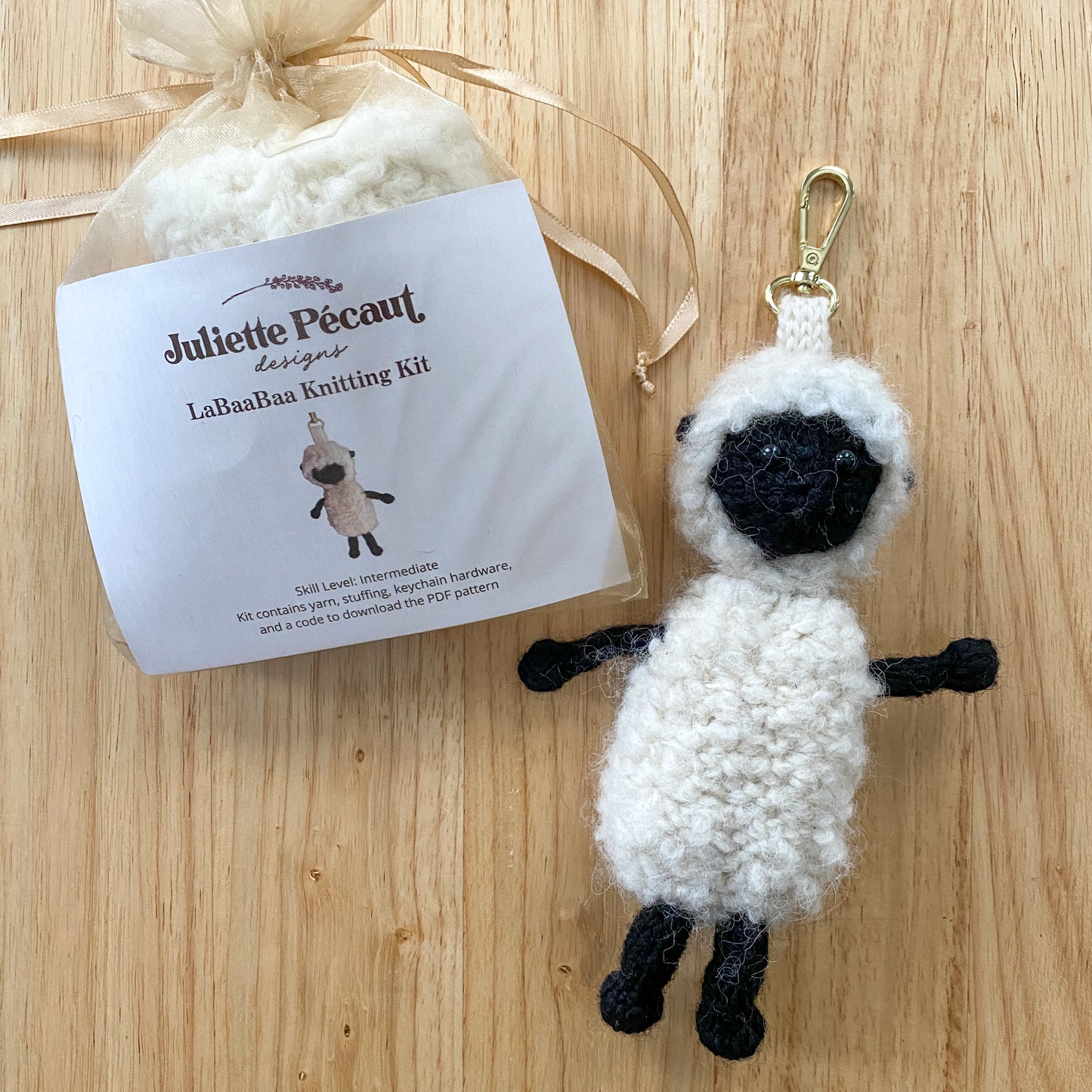 Knitted sheep keychain with a Juliette Pecaut knitting kit on a wooden surface