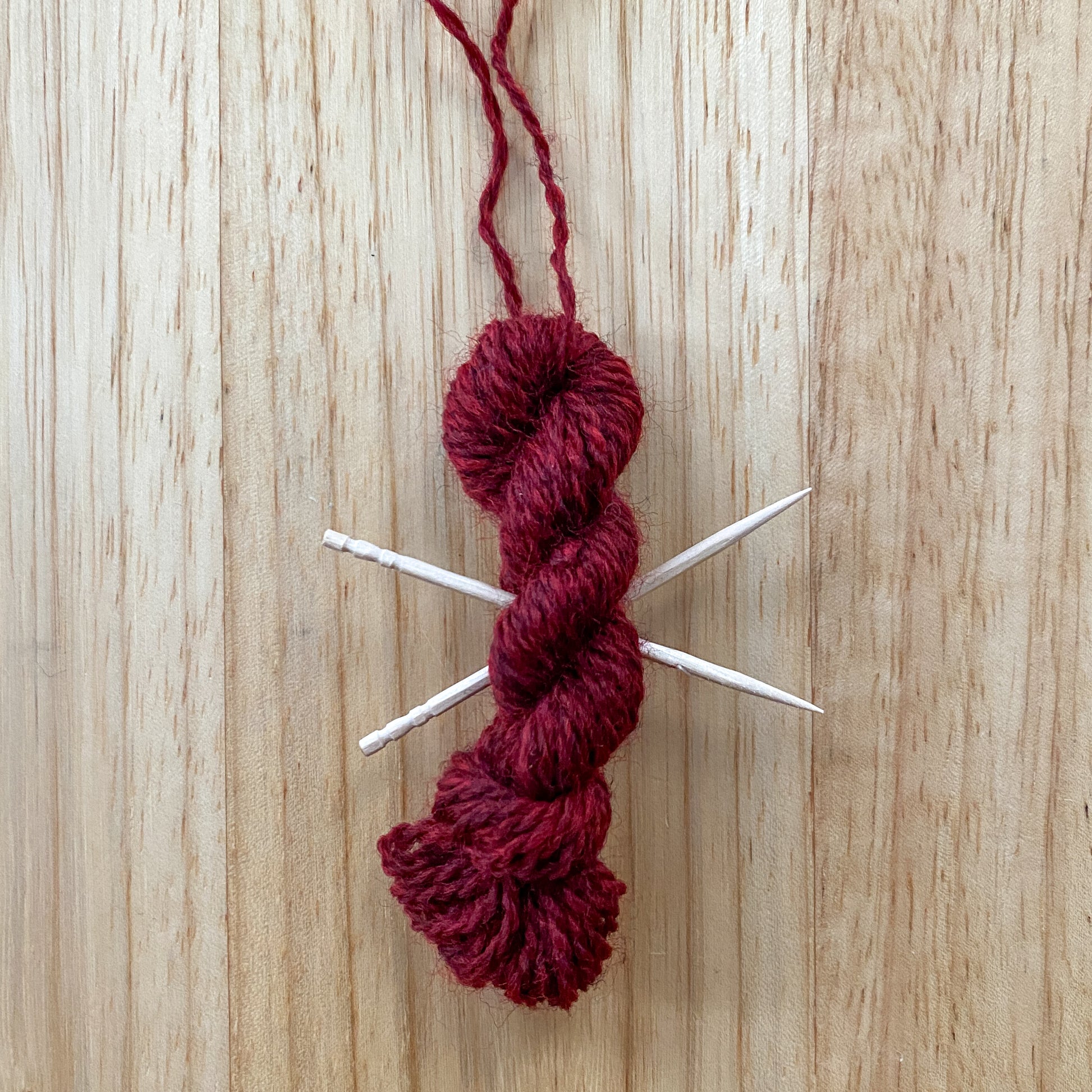 mini yarn skein ornament with toothpick knitting needles in maroon red