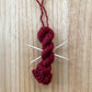mini yarn skein ornament with toothpick knitting needles in maroon red