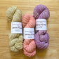 3 skeins of merino wool yarn in green, coral, and purple