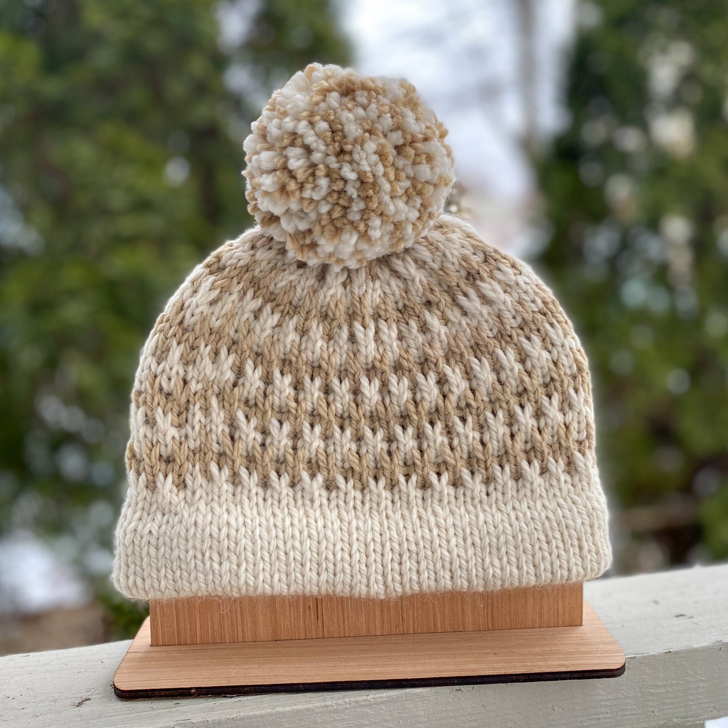 Knitted beanie with pom-pom on a wooden stand against a snowy background