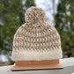 Knitted beanie with pom-pom on a wooden stand against a snowy background