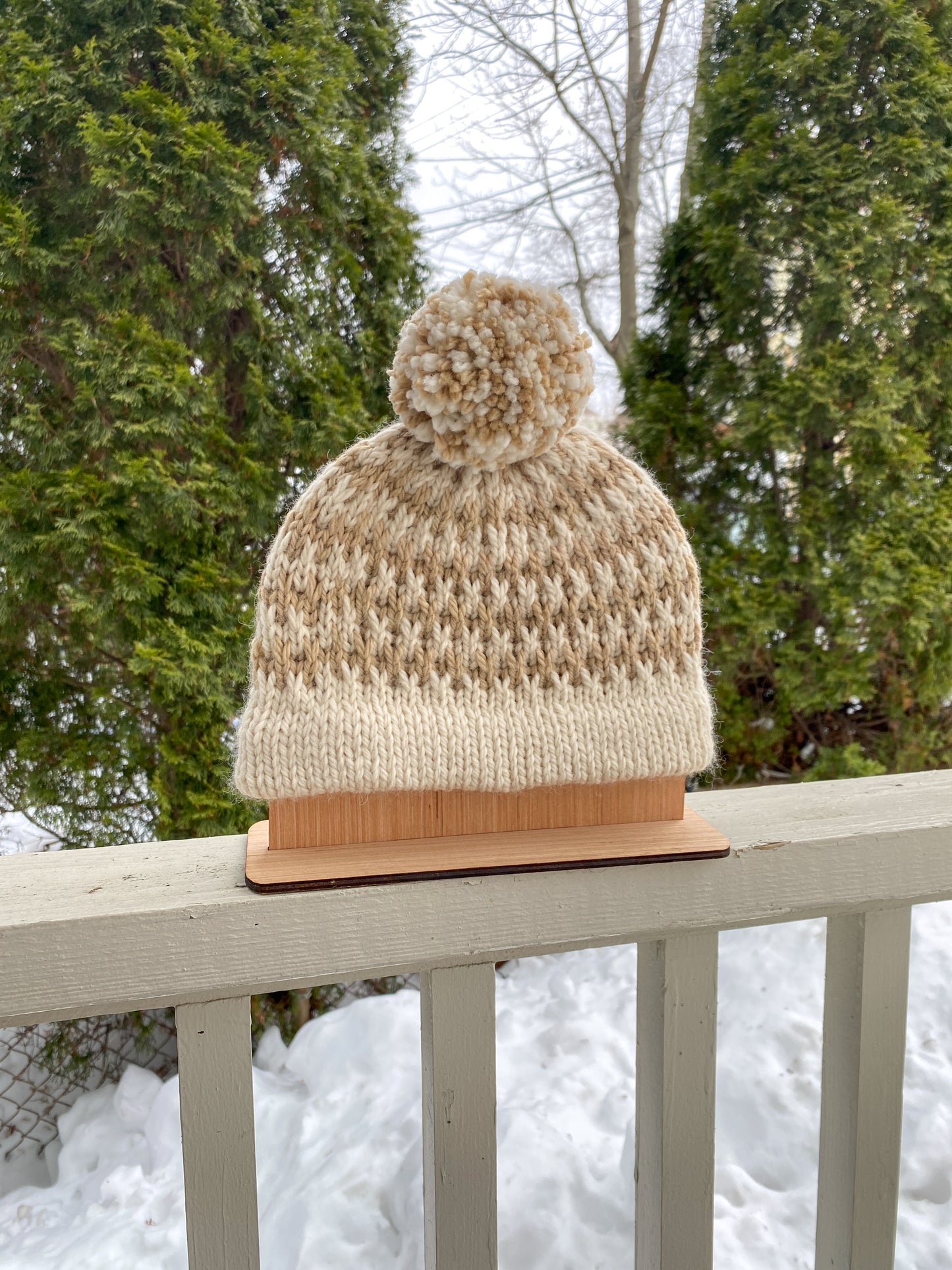 Knitted beanie with a pom-pom on a wooden stand against a snowy background