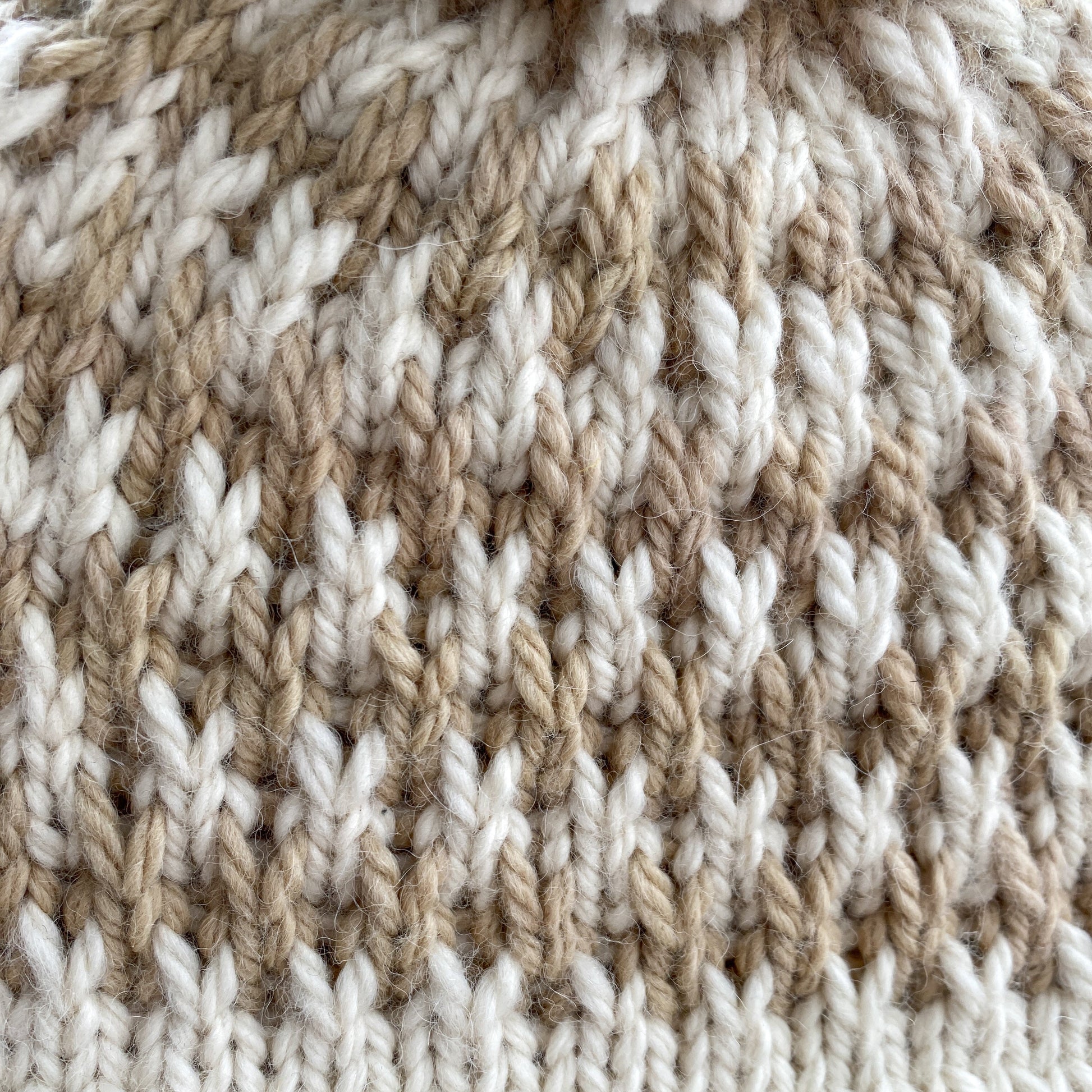 Close-up of a knitted fabric with a slipped stitch pattern of white and beige yarn.