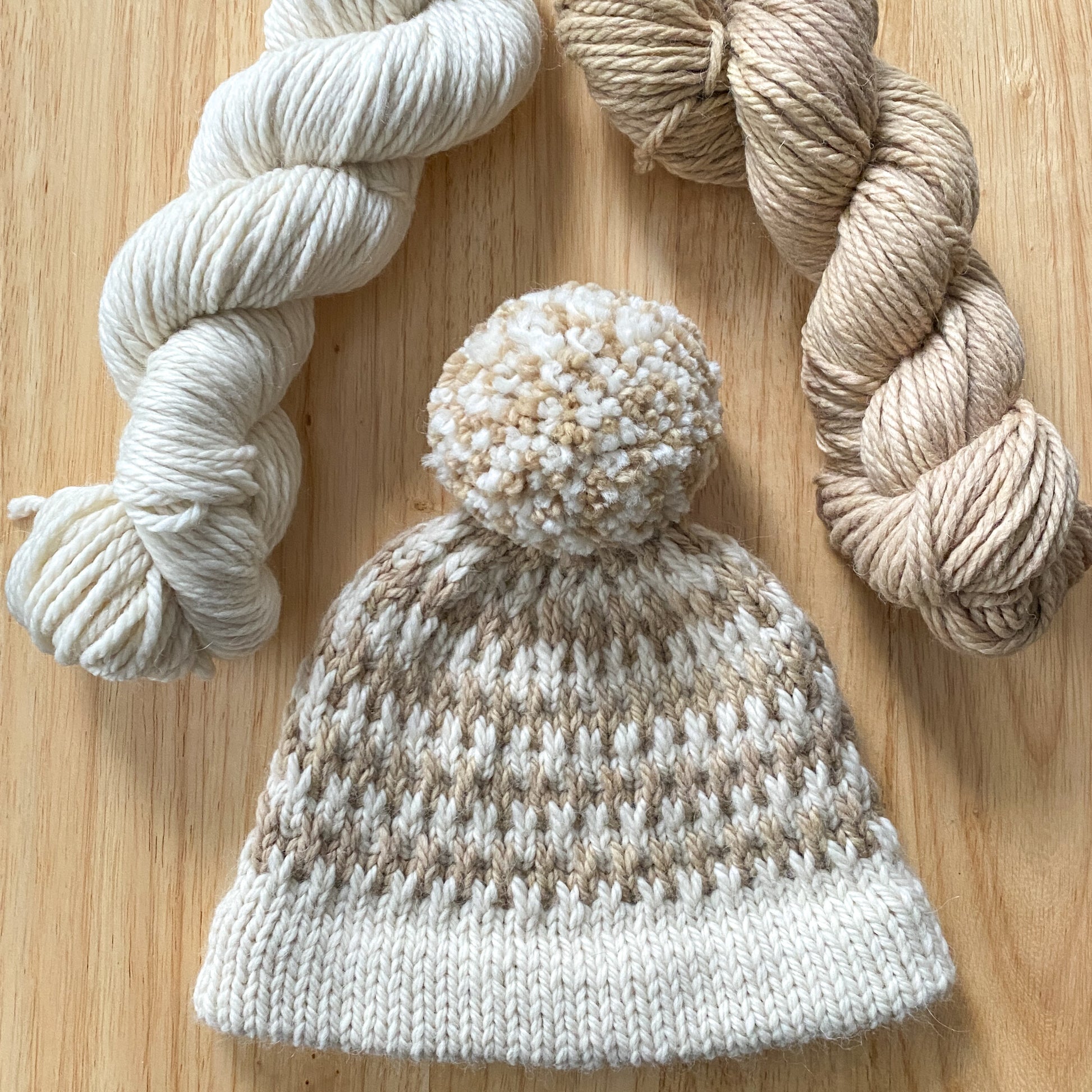 Knitted hat with pom-pom and yarn on a wooden surface