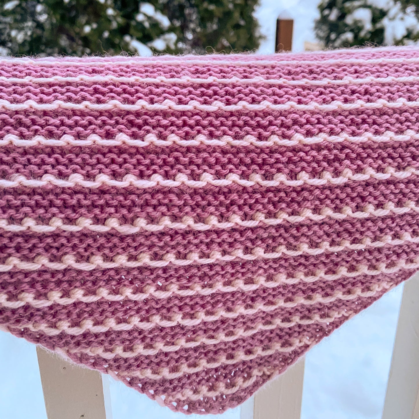 Pink and white striped knitted bandana scarf on a wooden surface with a snowy outdoor background