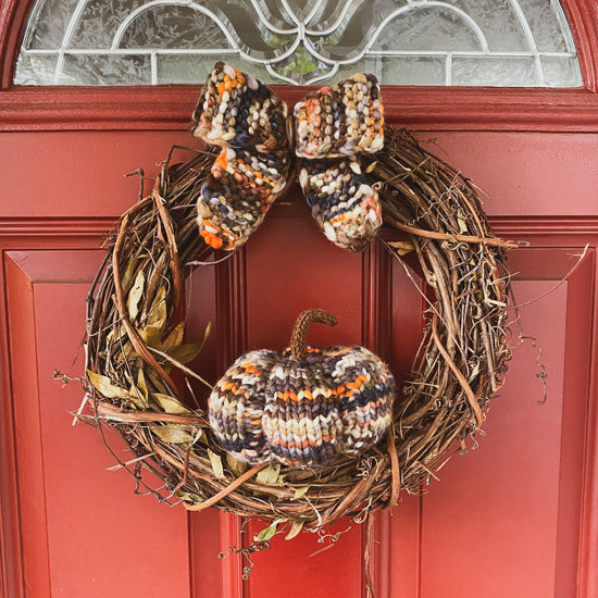 Decorative wreath with knitted bow and knitted pumpkin against a red door