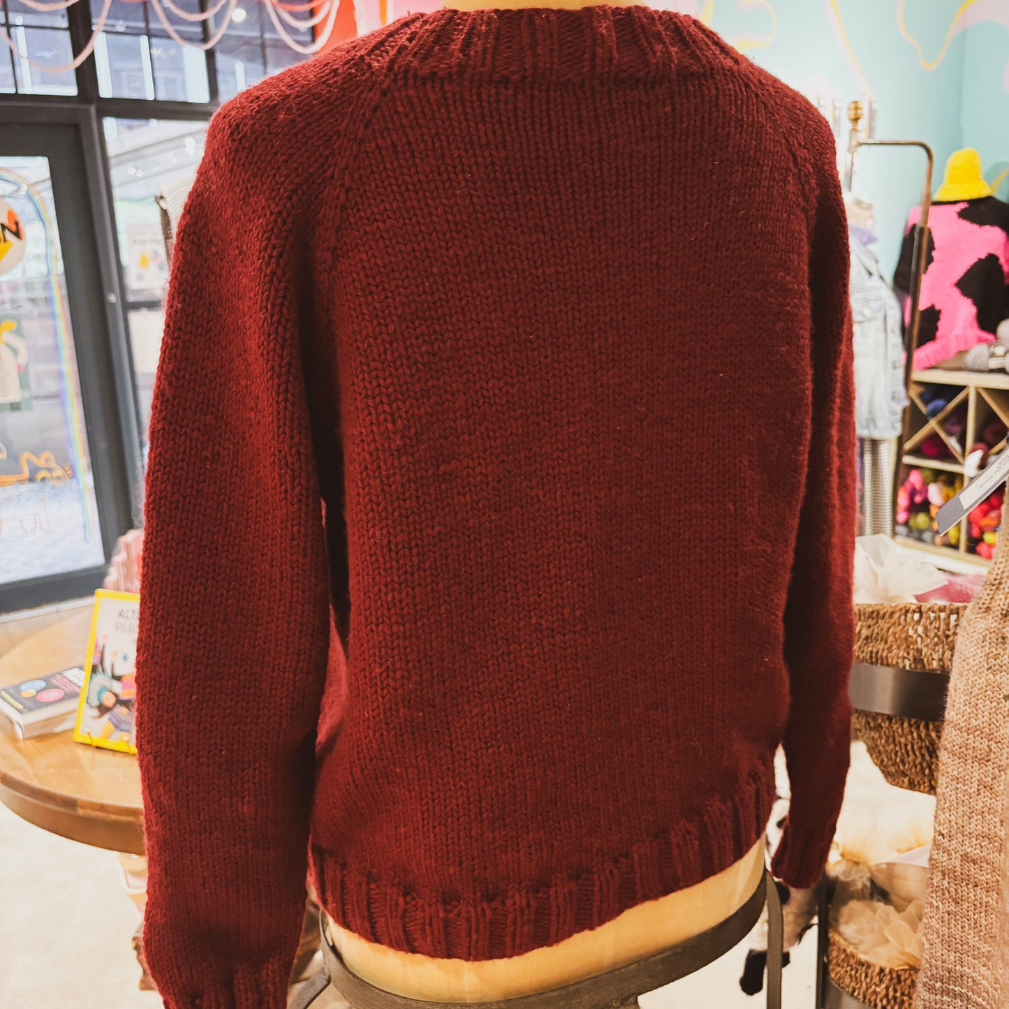 Mannequin wearing a red sweater in a store setting with colorful walls and various items.