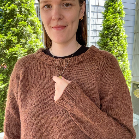Person wearing a brown sweater outdoors with greenery in the background