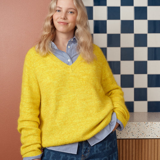 Person wearing a bright yellow sweater with a checkered wall background