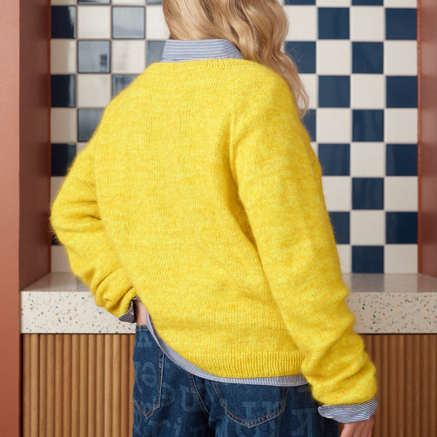 Person wearing a yellow sweater standing in front of a checkered wall.