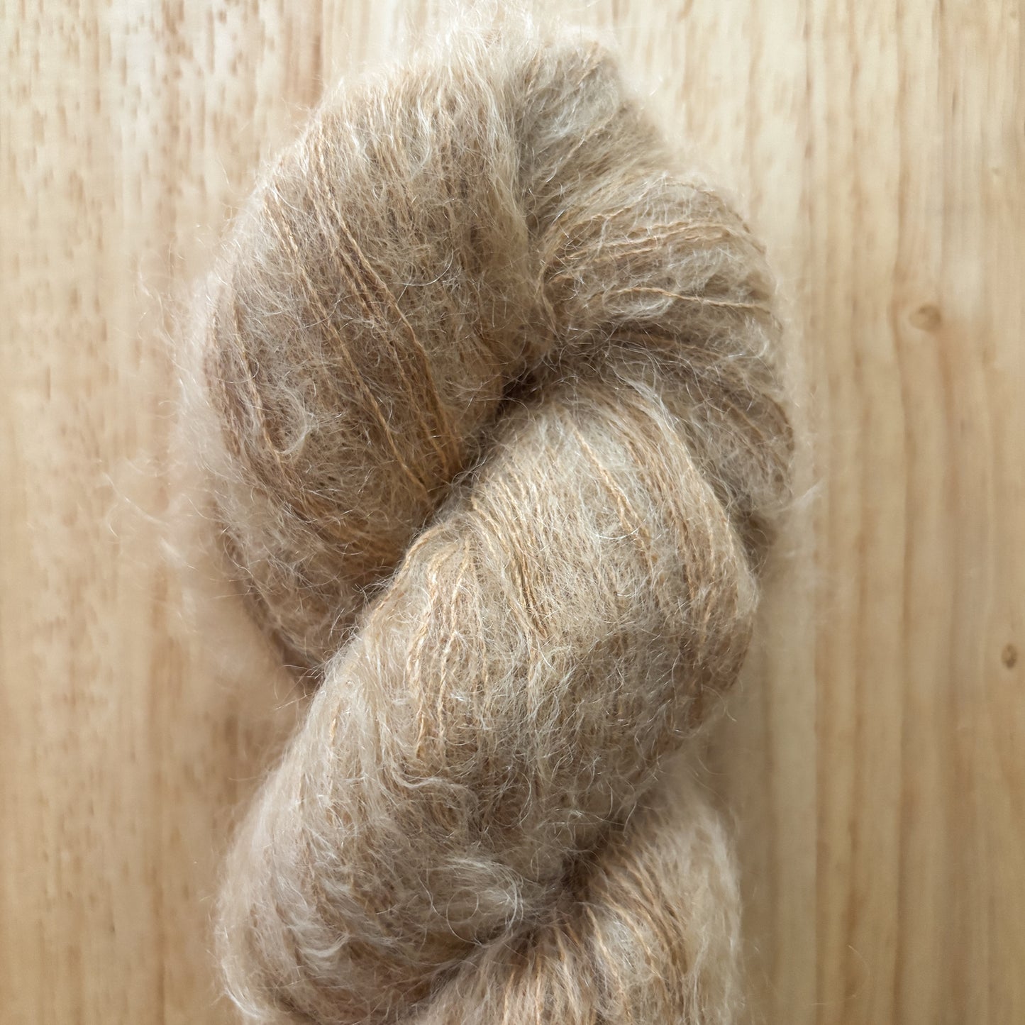 skein of fluffy light brown yarn on a wood surface