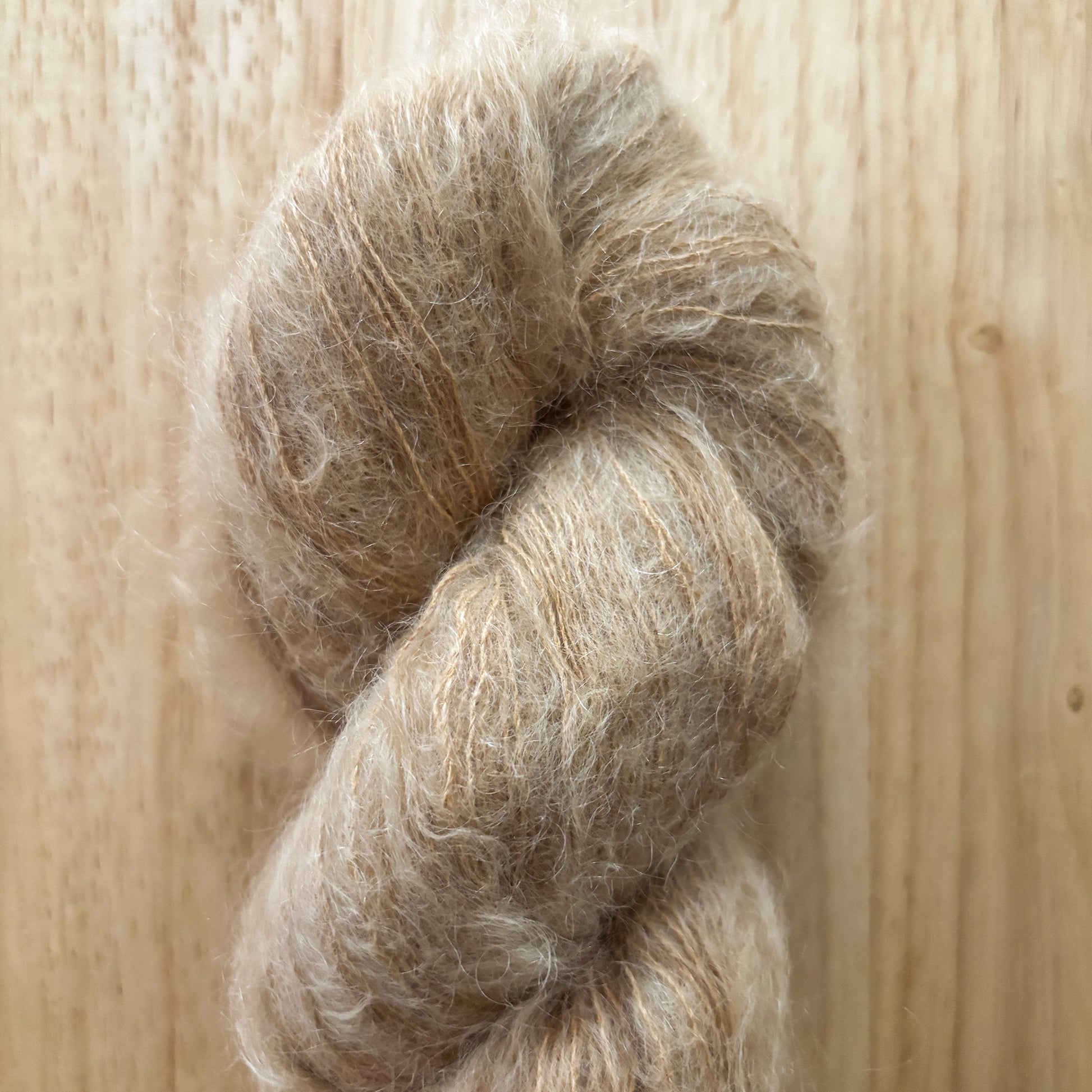 skein of fluffy light brown yarn on a wood surface