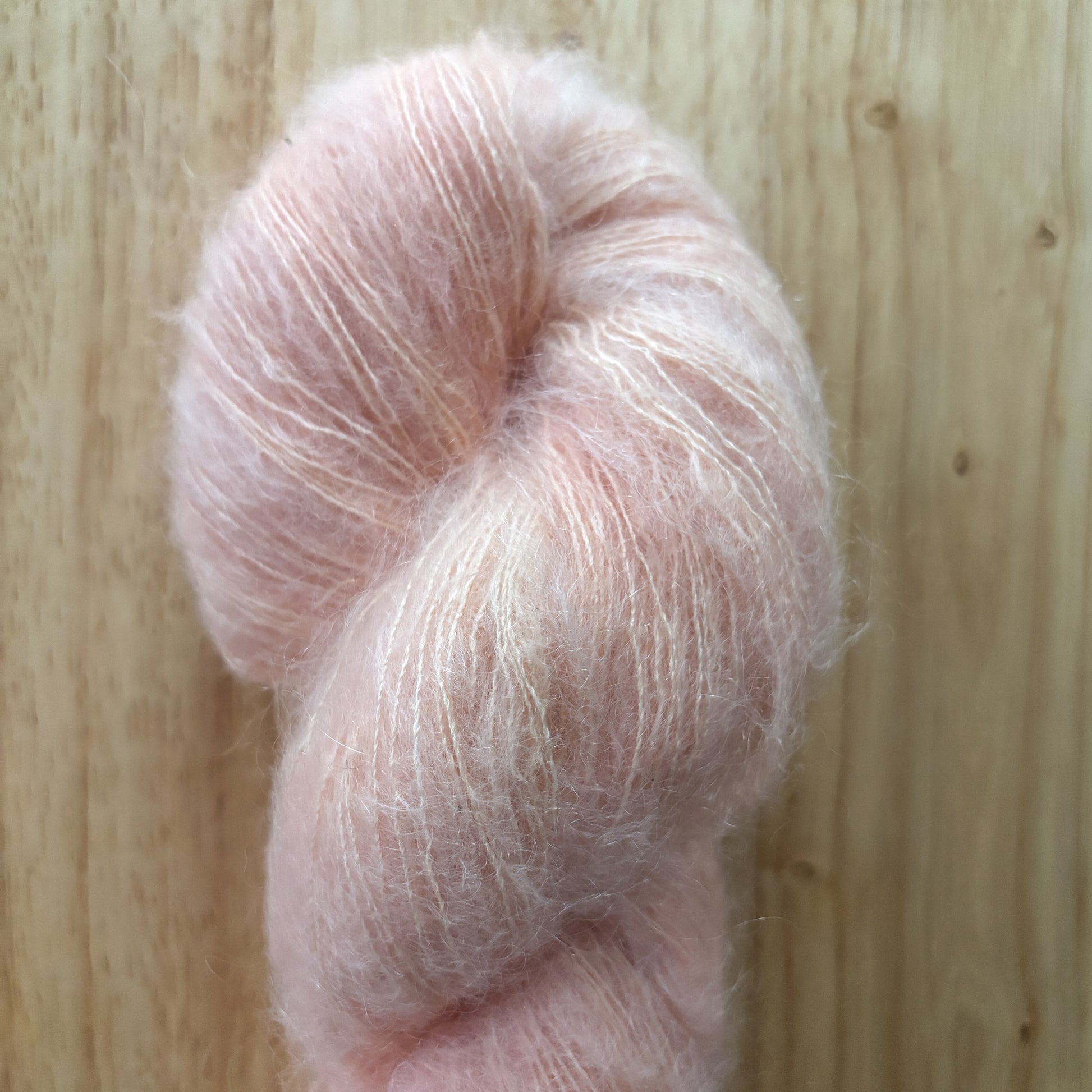 skein of fluffy light pink yarn on a wood surface