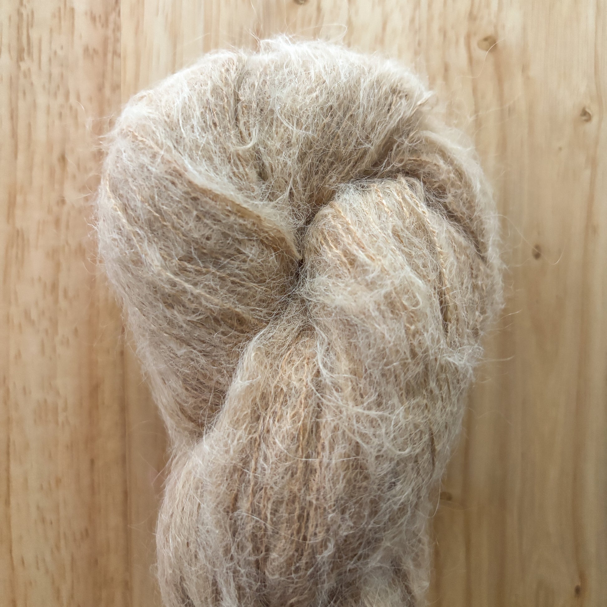 skein of fluffy light brown yarn on a wood surface